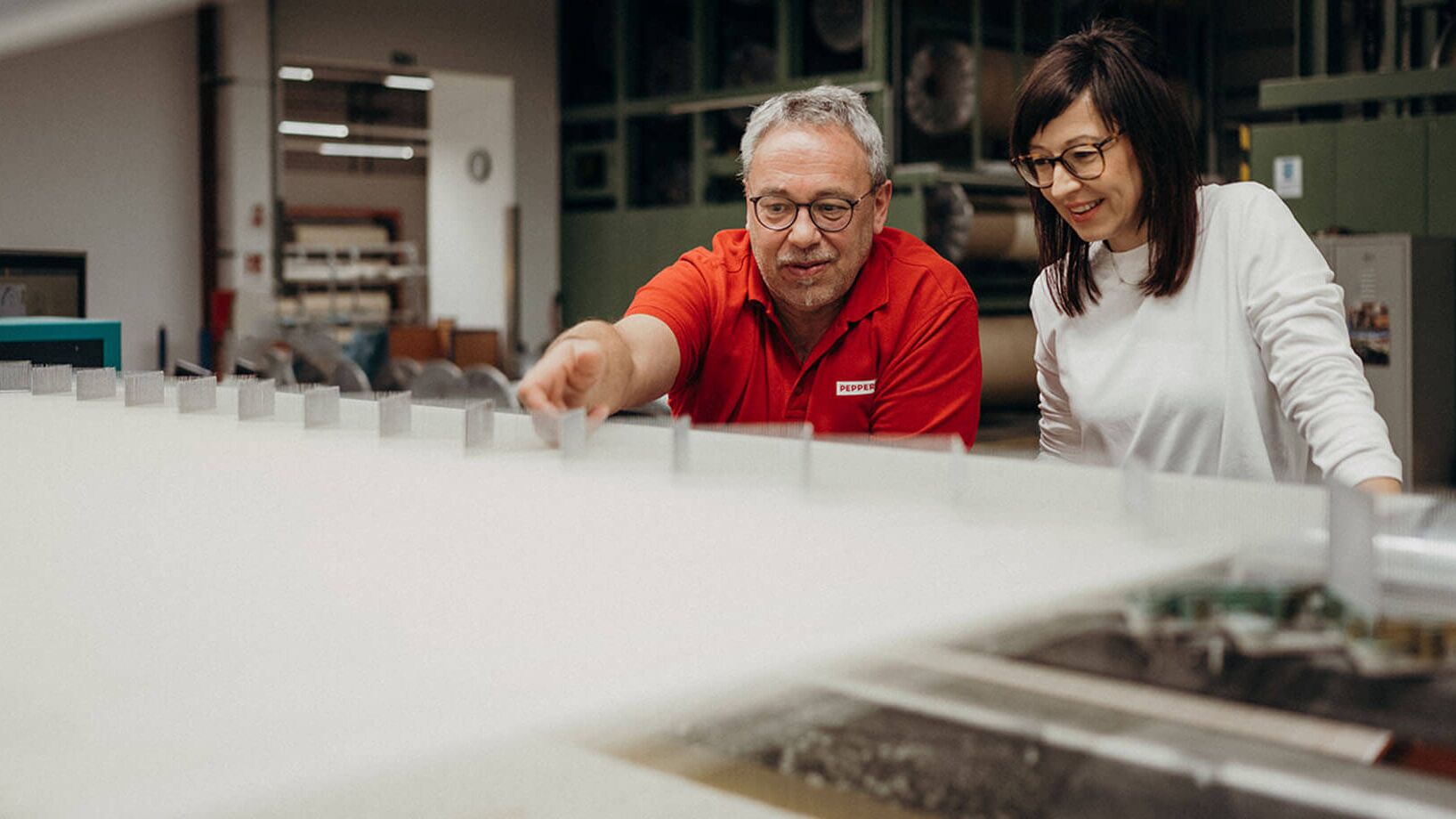 Two people examine a large sheet of material in a factory setting, showcasing Ertex's innovative products.
